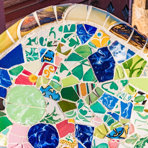 Primer plano de una colorida pared de mosaico con varios azulejos de forma irregular con dibujos verdes, azules, amarillos y rojos.