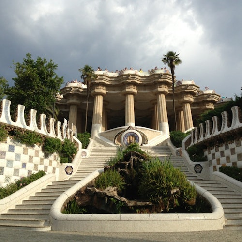 Gran escalera de piedra que conduce a una estructura ornamentada con columnas, flanqueada por paredes de azulejos de mosaico y vegetación.