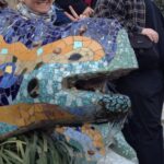 Gente posando detrás de una colorida escultura de lagarto en mosaico, con una persona mostrando un signo de la paz en el Parque Güell.