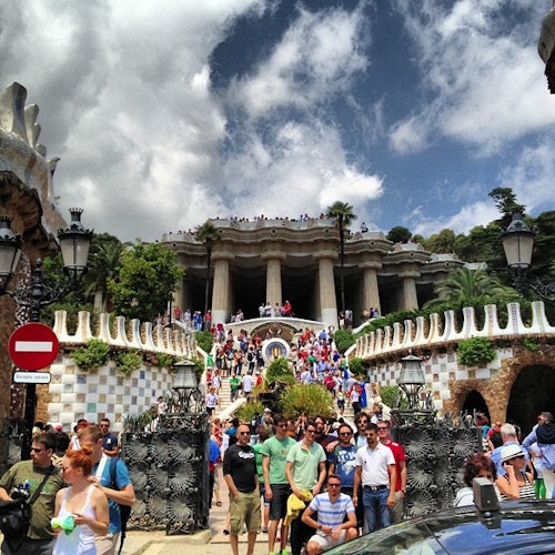 Multitud de personas ante una gran escalinata con barandillas decorativas, que conduce a una gran columnata bajo un cielo parcialmente nublado.