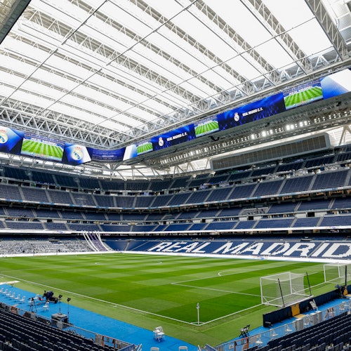An empty football stadium with a green field, stands displaying 'Real Madrid,' and a partially closed roof.