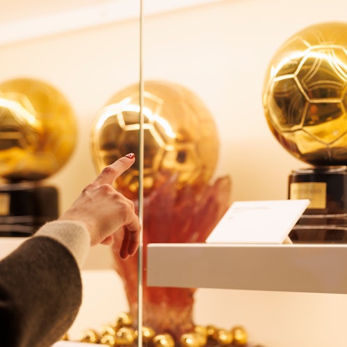 Person pointing at a golden soccer ball trophy displayed behind glass.