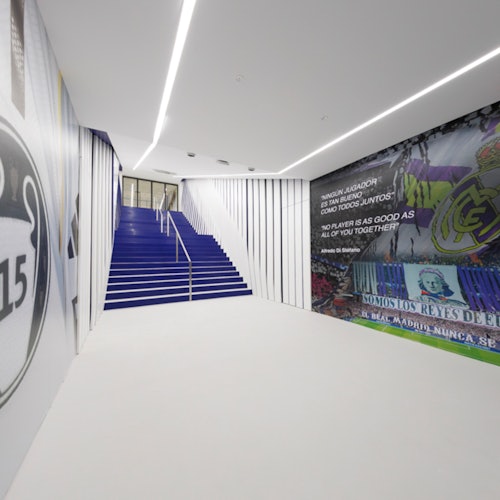 A modern hallway with white walls, a blue staircase, and walls adorned with sports-related murals and text.