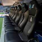 A row of black leather stadium seats with BMW and Real Madrid logos, positioned on a sports field's sideline.