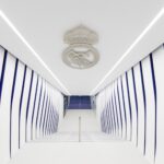A white and blue hallway with striped walls and a ceiling emblem, leading to stairs in the distance.