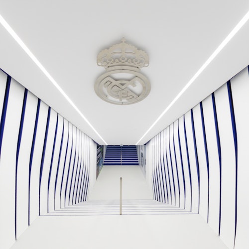 A white and blue hallway with striped walls and a ceiling emblem, leading to stairs in the distance.