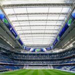 A large stadium with a retractable roof, LED screens, and a green football field, viewed from the goal area.
