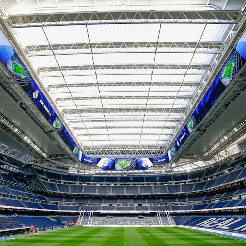 A large stadium with a retractable roof, LED screens, and a green football field, viewed from the goal area.