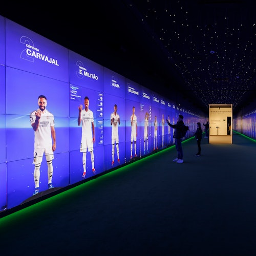 A futuristic display wall showing life-sized images of soccer players in a dimly lit room with visitors interacting.