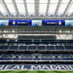 A view of an empty stadium with "Real Madrid C.F." displayed on large screens and "Real Madrid" written on the seating.