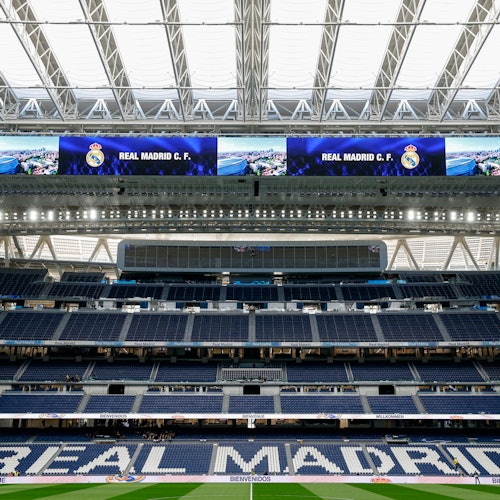 A view of an empty stadium with "Real Madrid C.F." displayed on large screens and "Real Madrid" written on the seating.